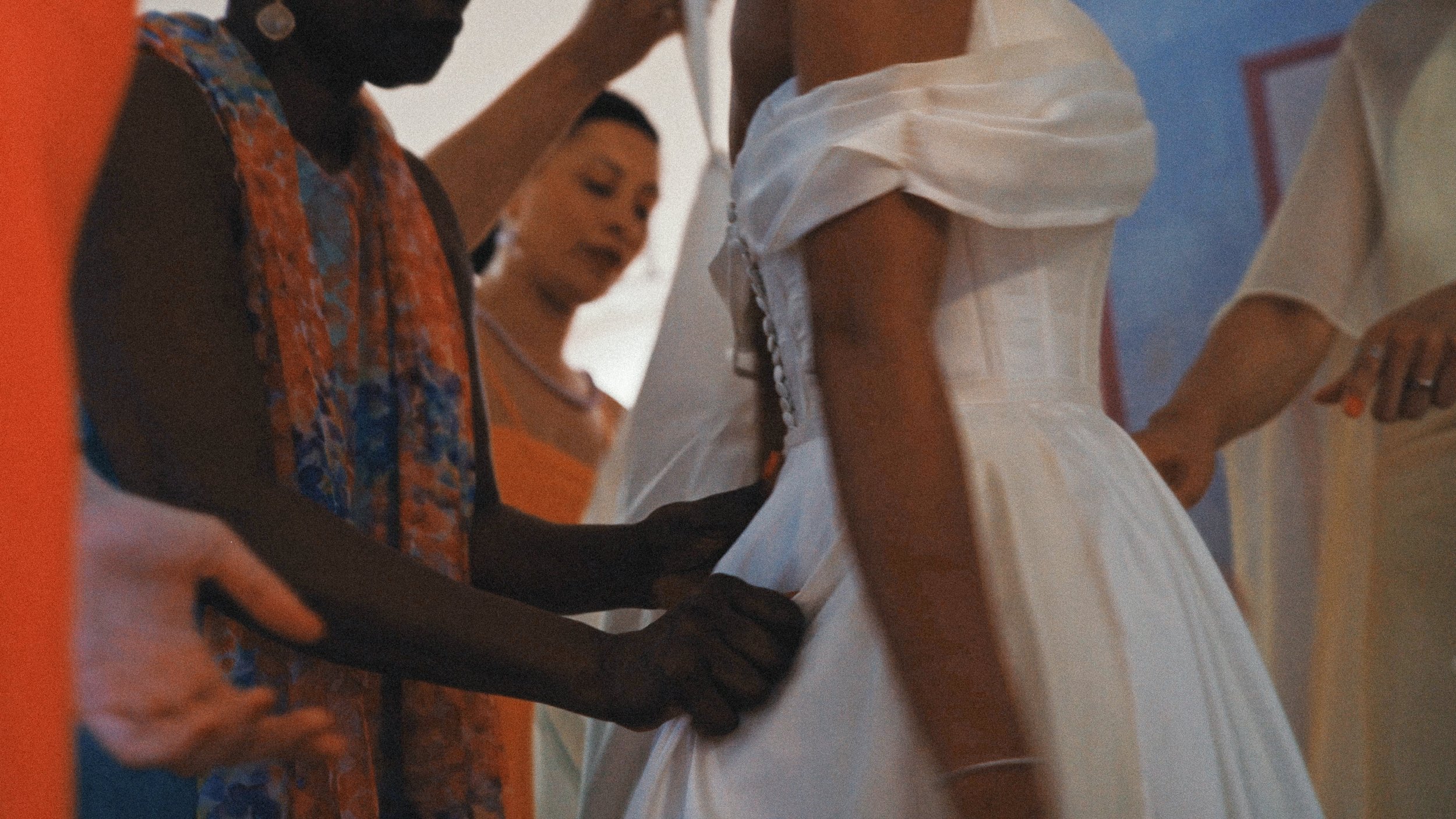 Une femme en train de faire une robe blanche, entourée de plusieurs personnes lors d'une séance de couture ou de création de vêtements.