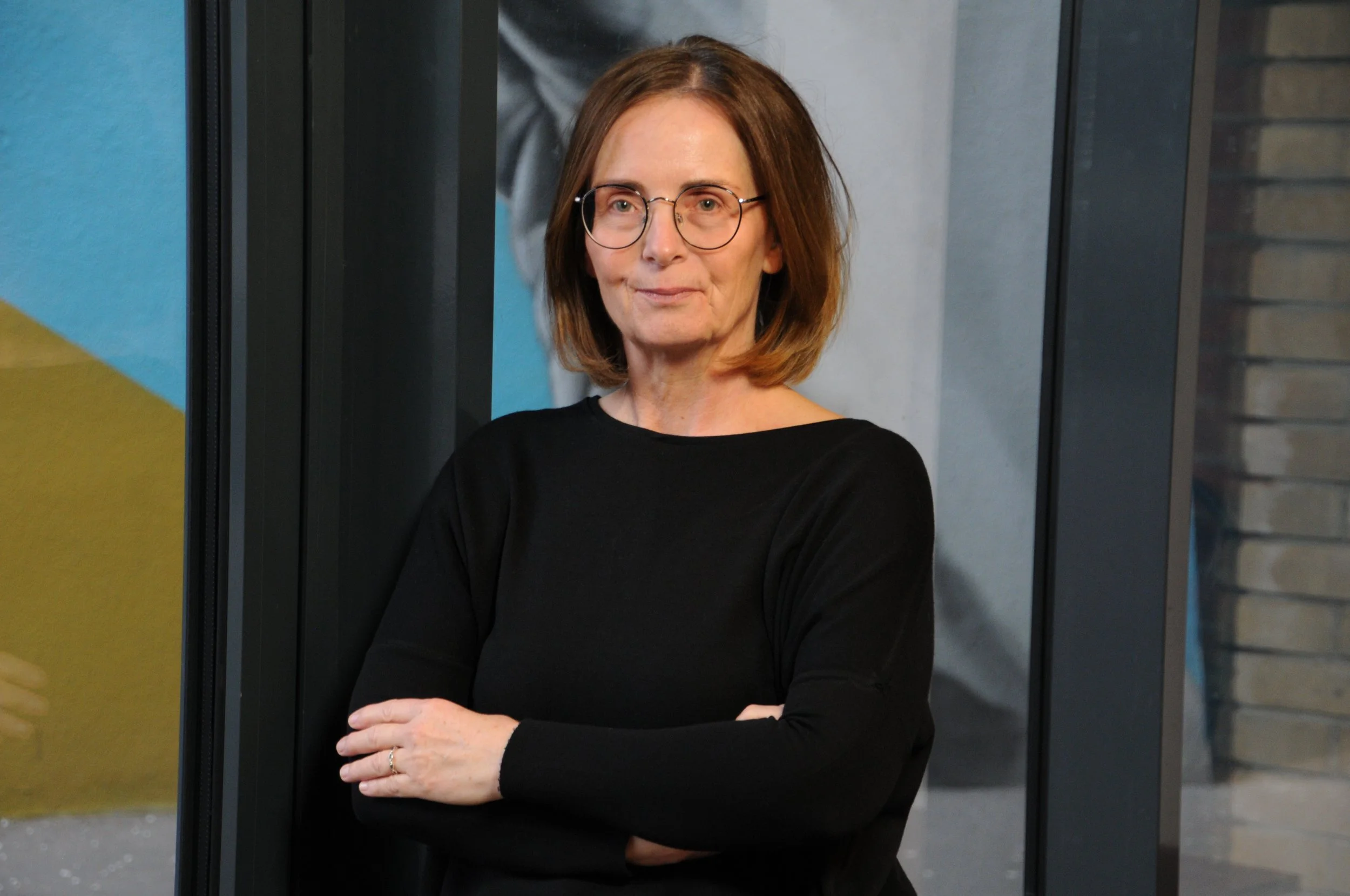 Frau mit mittellangen Haaren, feiner Brille und schwarzem Pullover schaut in die Kamera