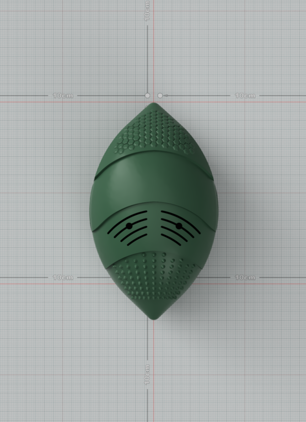 A green lemur-shaped object with textured and slotted surfaces, lying on grid paper marked with 10cm measurements.