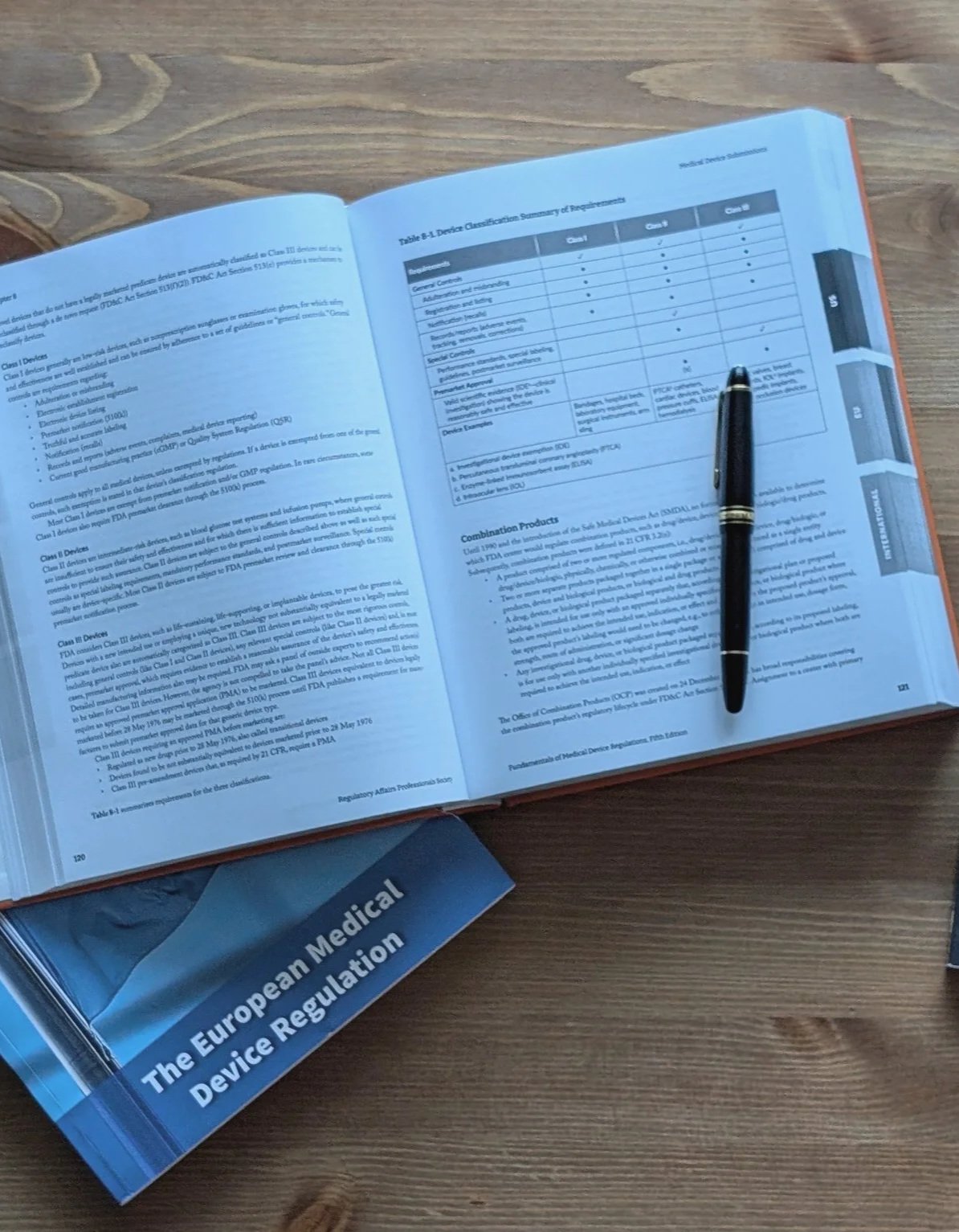 Open book titled 'The European Medical Device Regulation' on a wooden table, with a pen resting on the right page.