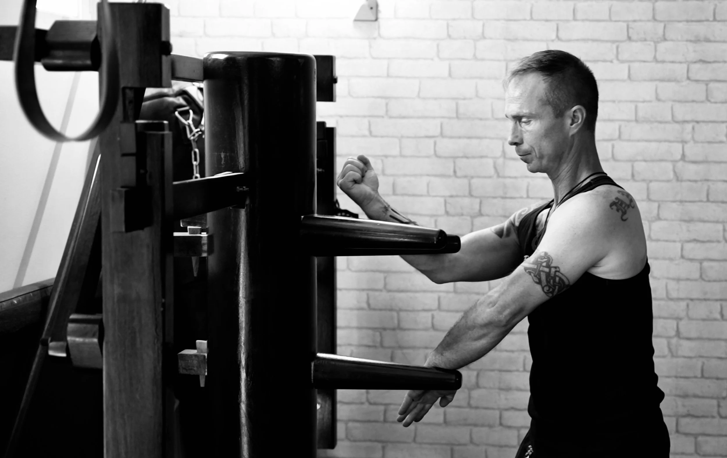Un homme musclé s'entraîne avec un punching ball dans une salle de sport en noir et blanc.
