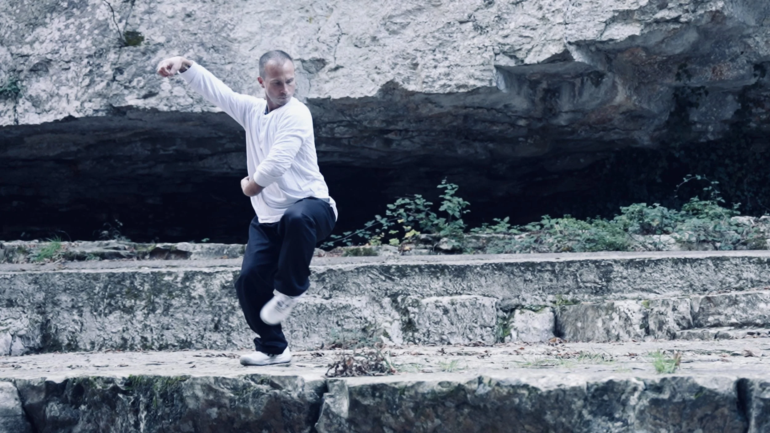 Un homme pratique le tai chi en extérieur sur des marches en pierre, avec une falaise en arrière-plan.