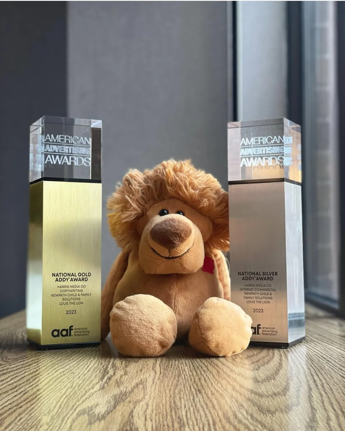 A stuffed lion toy sitting between two American Advertising Federation awards on a wooden surface.