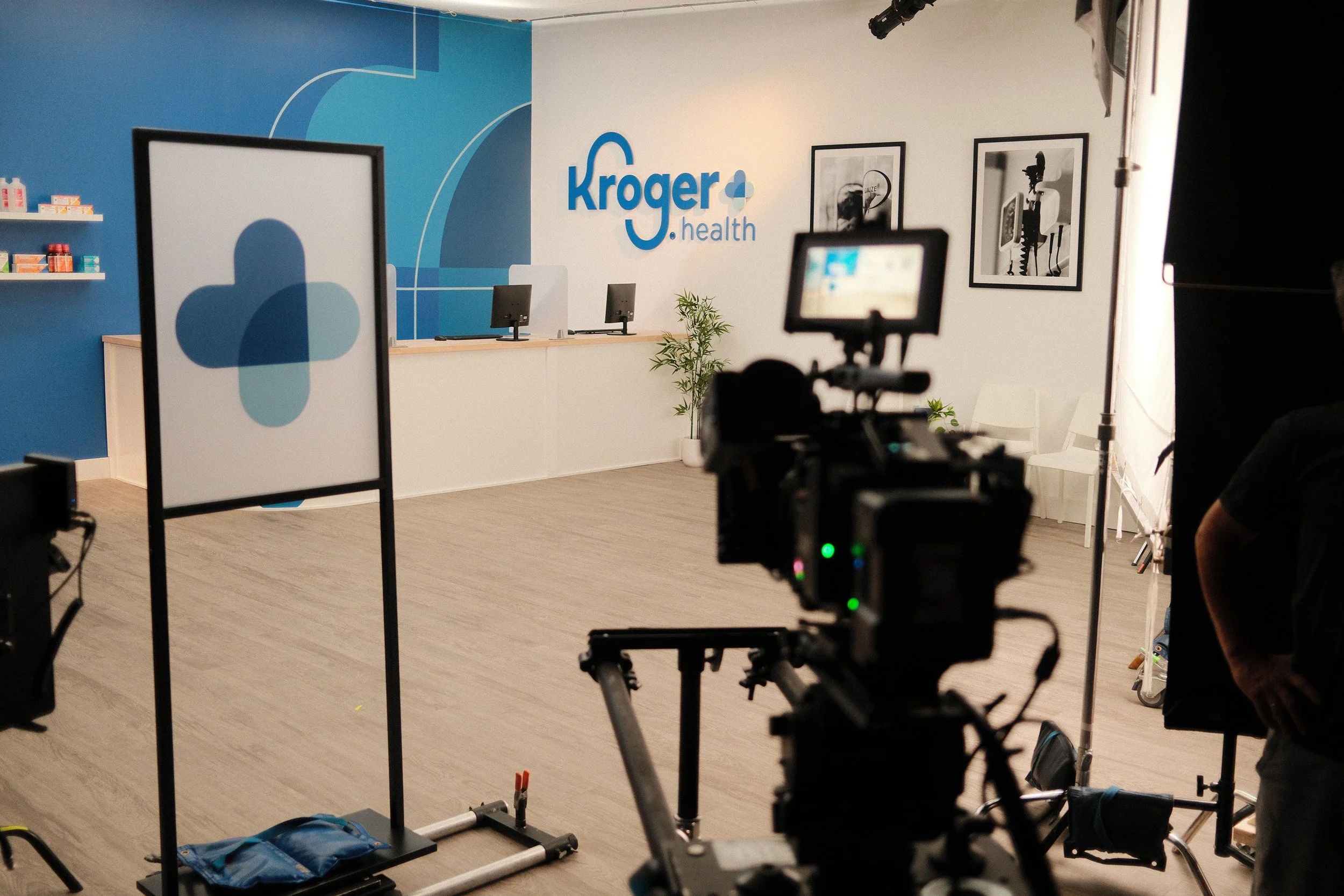 Behind the scenes of a video shoot at Kroger Health, with cameras, lighting equipment, and a backdrop with the Kroger logo and health-themed decor.
