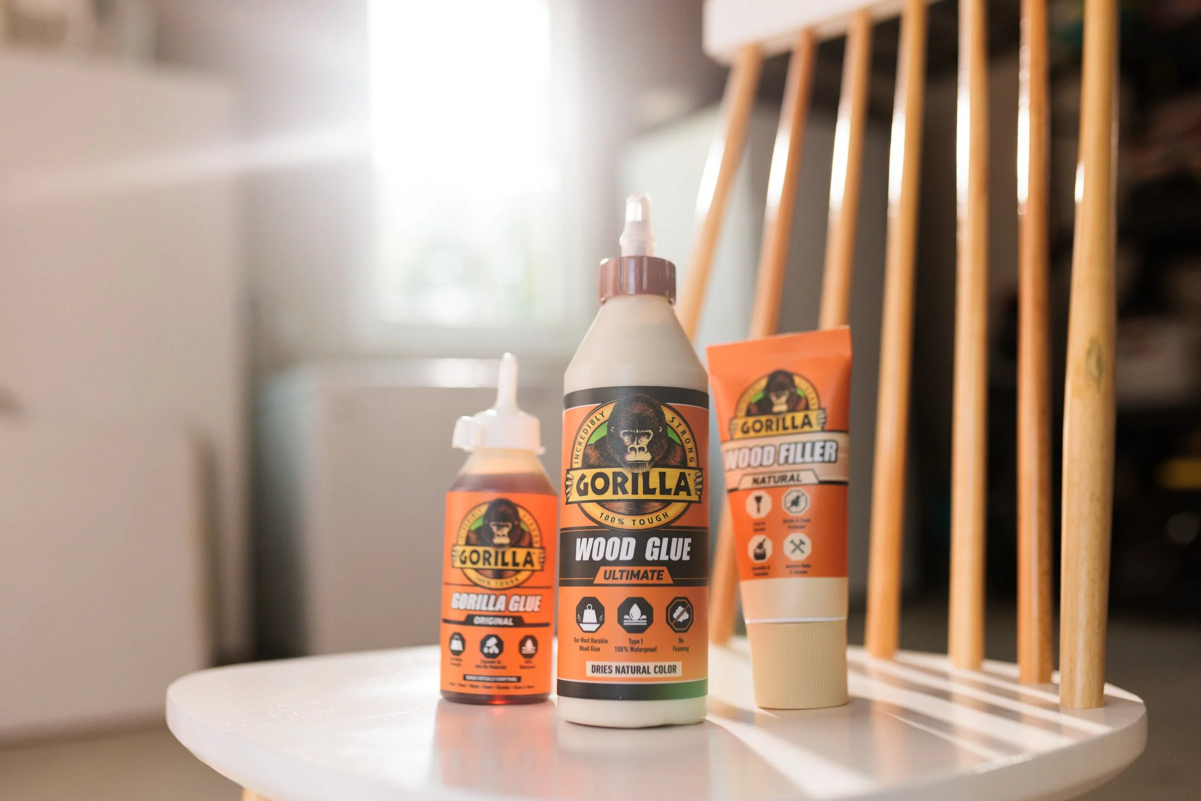 Three Gorilla wood glue bottles and tubes on a white table in a sunny room.