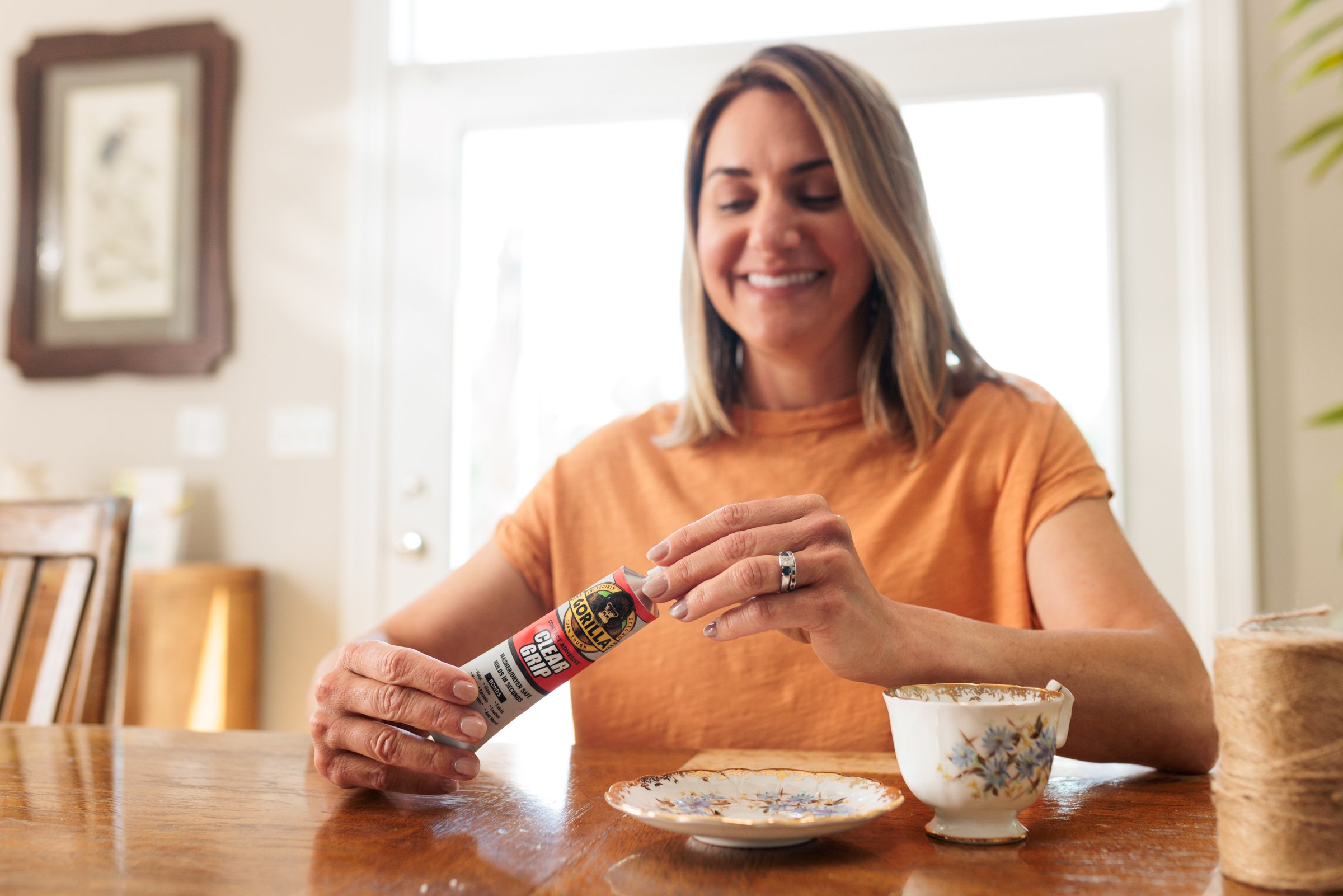 Woman smiling at a table, holding a can of bear spray near a teacup and saucer.