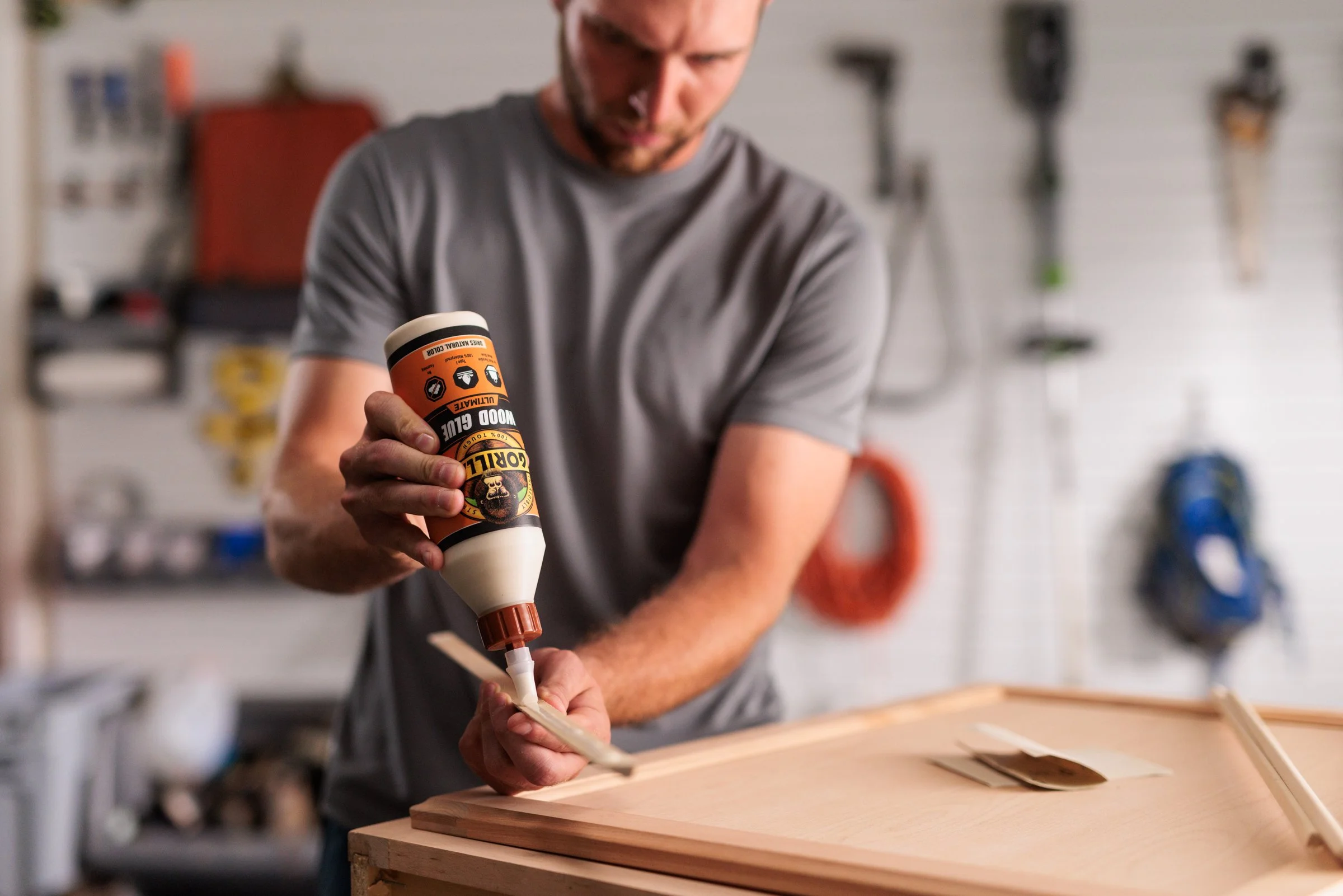 A man applying wood glue to a wooden surface in a workshop.