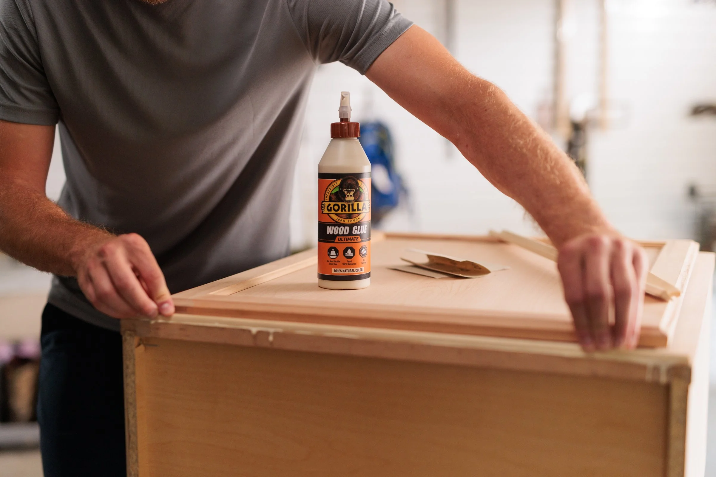 Person applying wood glue to a wooden piece, with a bottle labeled Gorilla Wood Glue on the work surface.