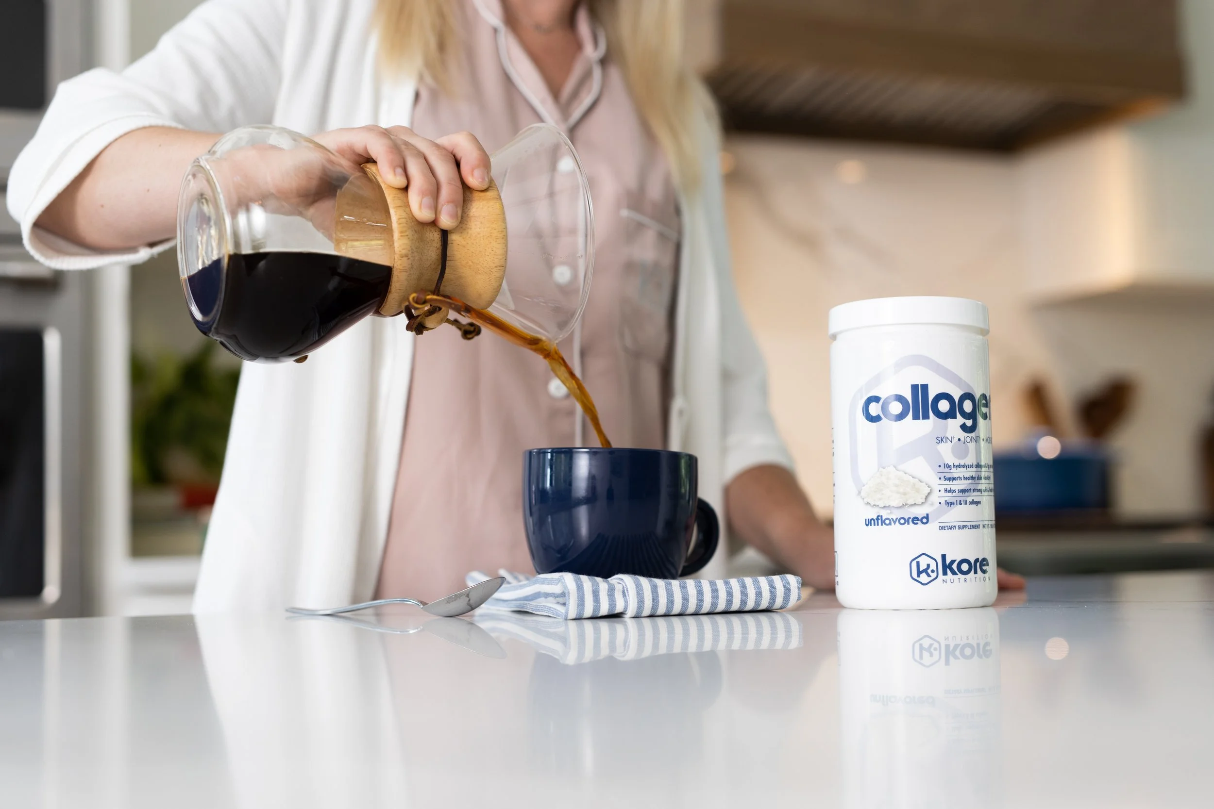 Person pouring coffee into a mug in a modern kitchen with a container of collagen powder on the counter.