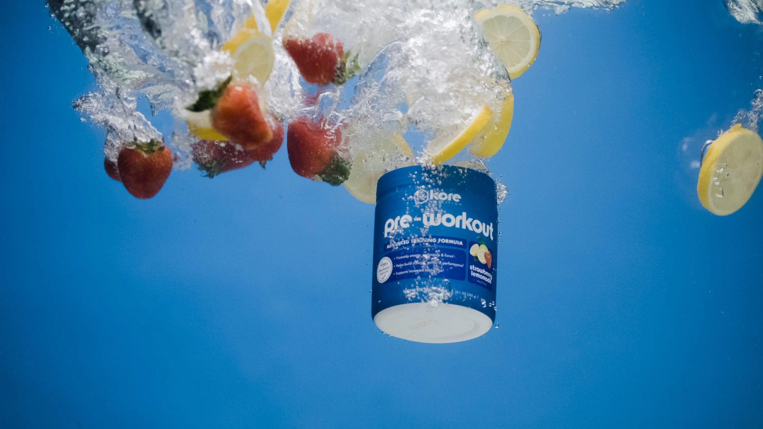 A container of pre-workout supplement falling into water with strawberries and lemon slices, creating a splash effect.