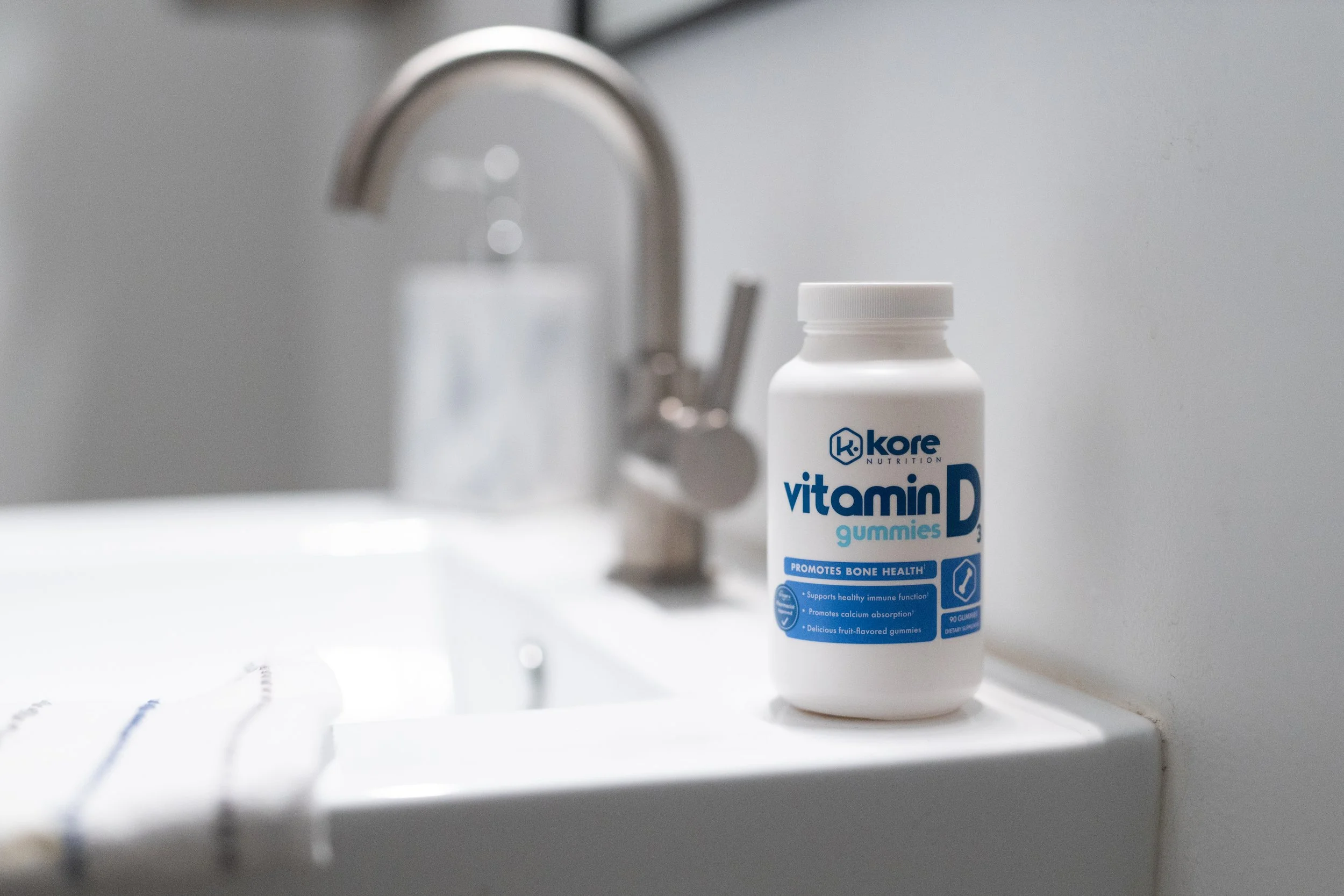 A bottle of KORE Nutrition vitamin D gummies on a white bathroom sink with a silver faucet in the background.
