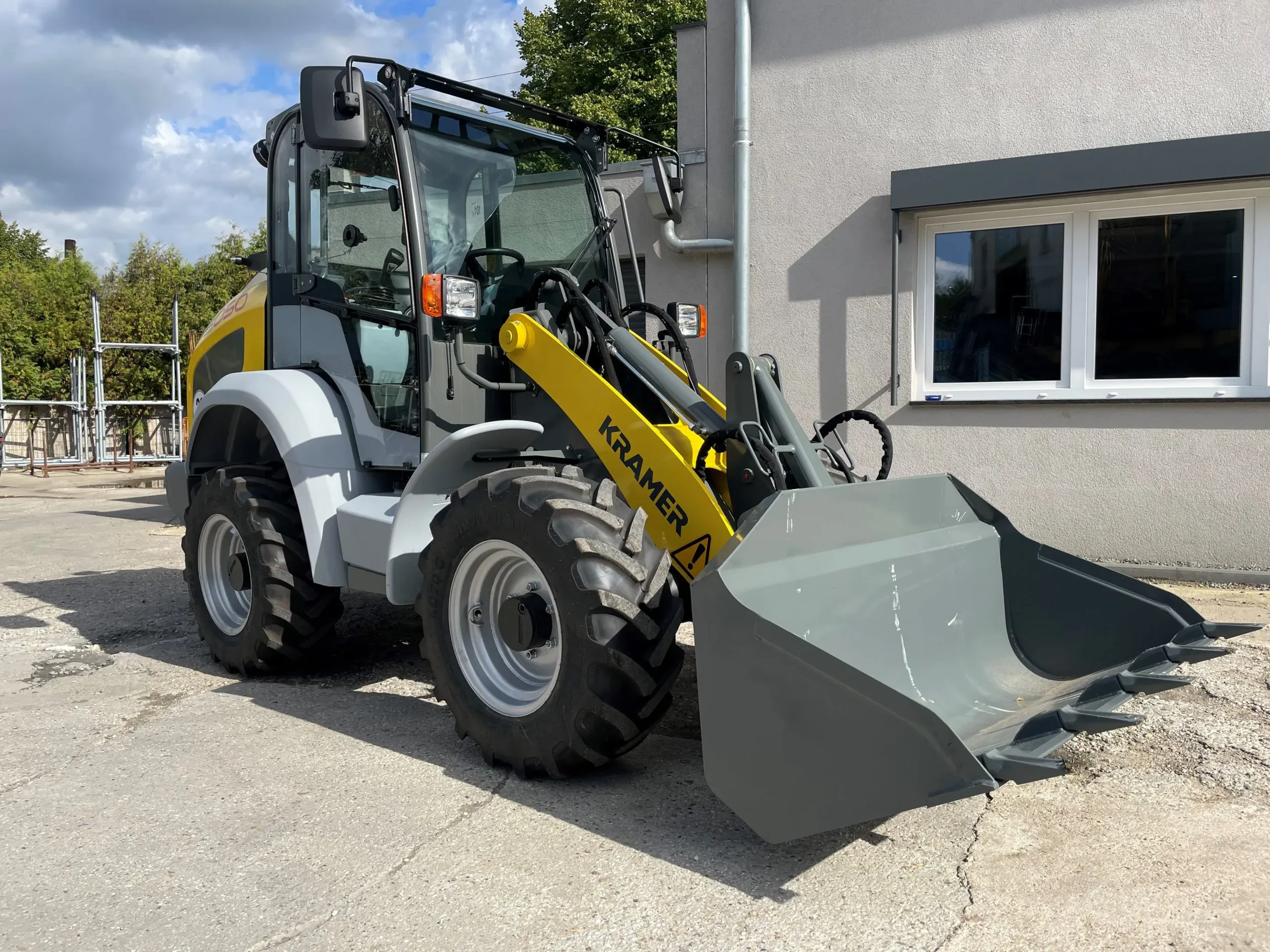 Leistungsstarker, gelb-grauer Radlader der Marke Kramer (Modell 5050) mit geschlossener Kabine, Allradlenkung und robuster Ladeschaufel mit Zähnen zur Miete.