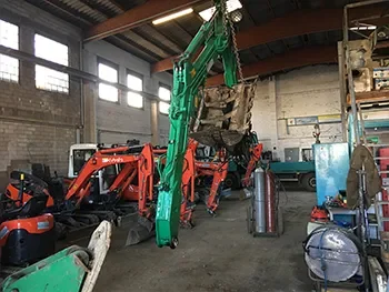Innenansicht einer Werkstatt mit grünem Kranarm und abgestellten Baumaschinen, aufgenommen während Wartungs- und Reparaturarbeiten.