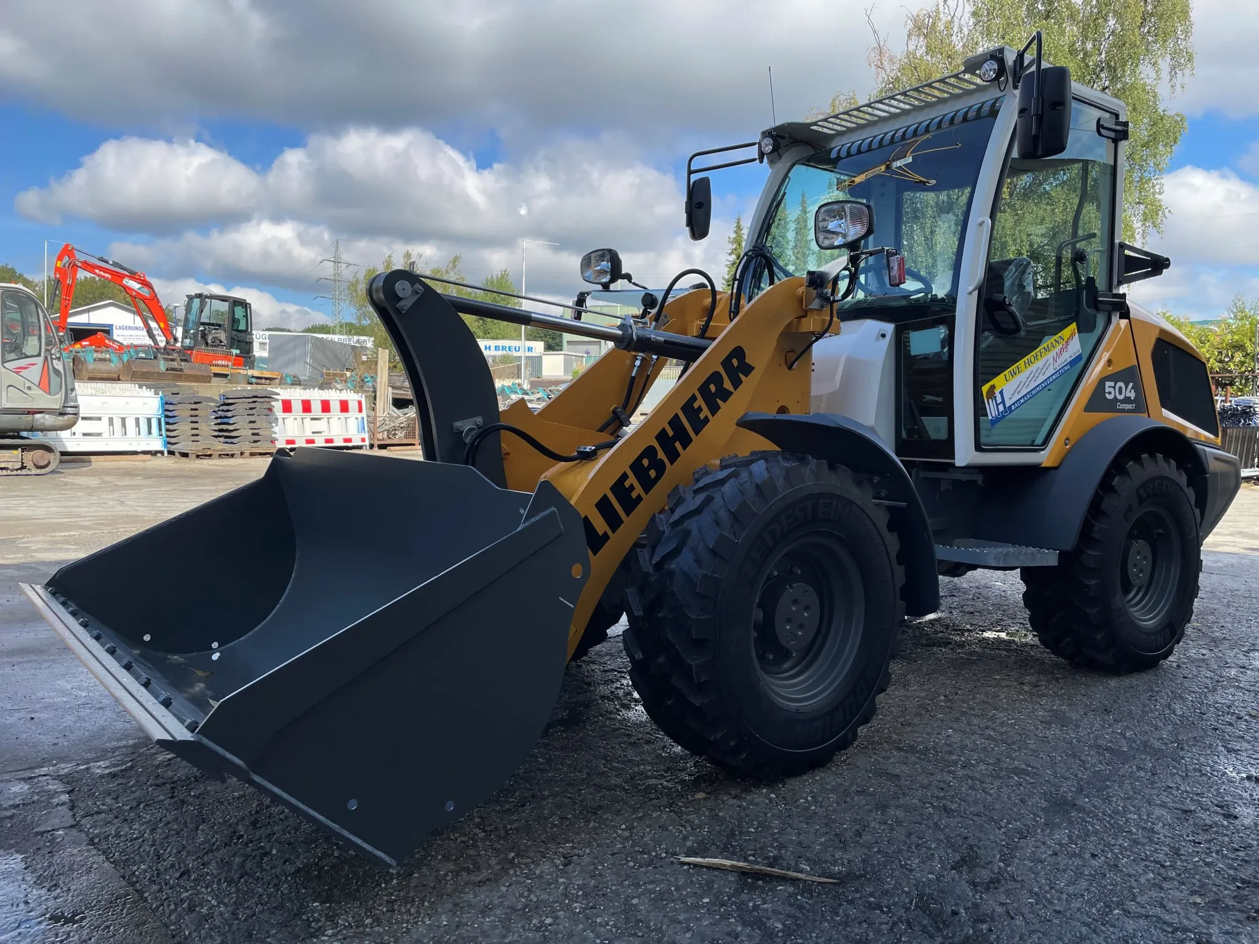 Leistungsstarker, gelb-weißer Kompaktradlader der Marke Liebherr (Modell L 504 Compact) mit geschlossener Kabine und breiter Ladeschaufel zur Miete für effiziente Lade-, Transport.