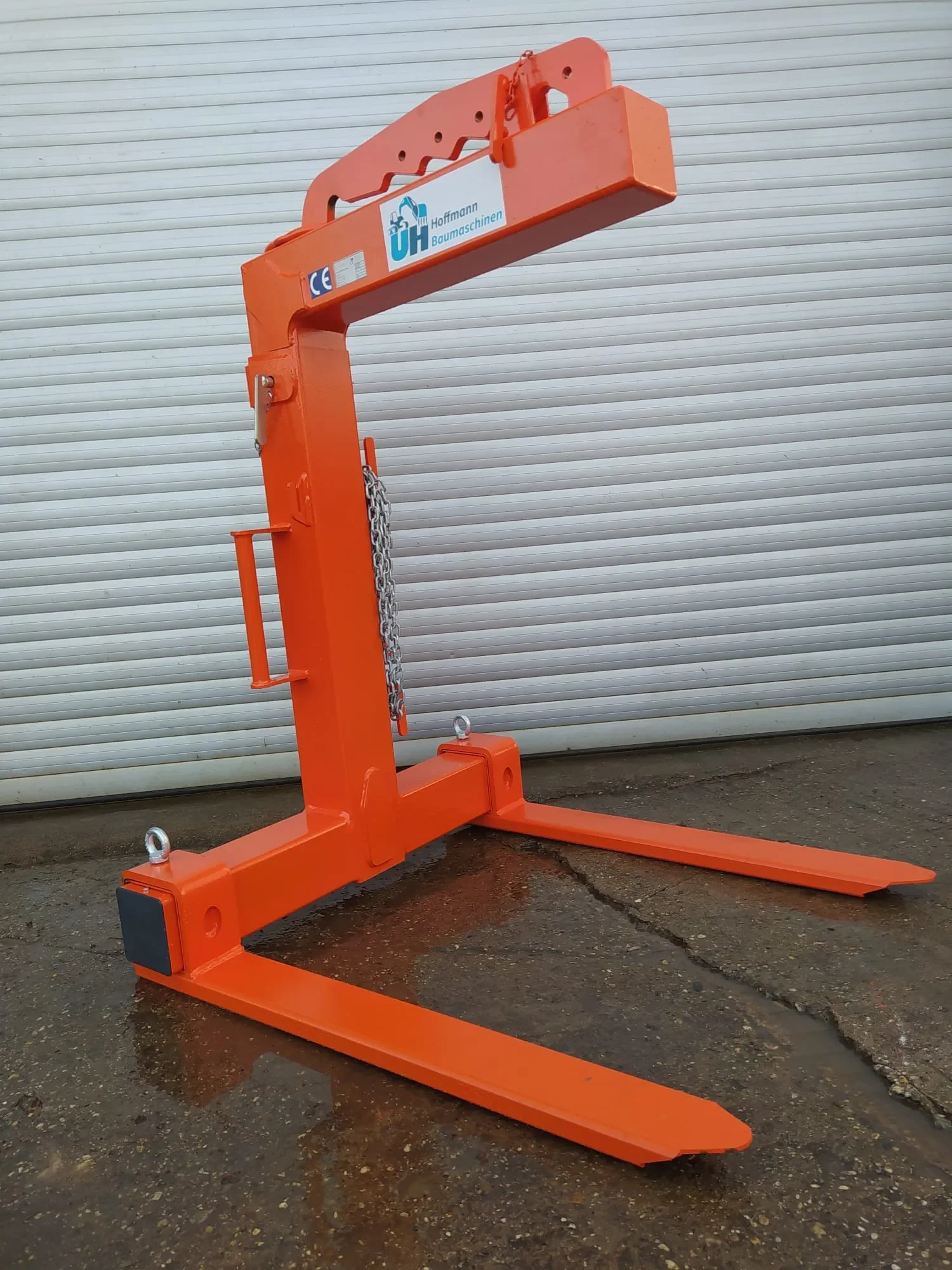 Orangefarbene Krangabel (Palettengabel) mit manuellem Gewichtsausgleich und Sicherungskette zur Miete für den sicheren und effizienten Transport von palettierten Baumaterialien per Kran auf Baustellen.