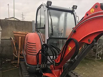 Frontansicht eines roten Minibaggers mit Ausleger und Hydraulikschläuchen auf dem Betriebshof, bereit für Wartung und Reparatur.