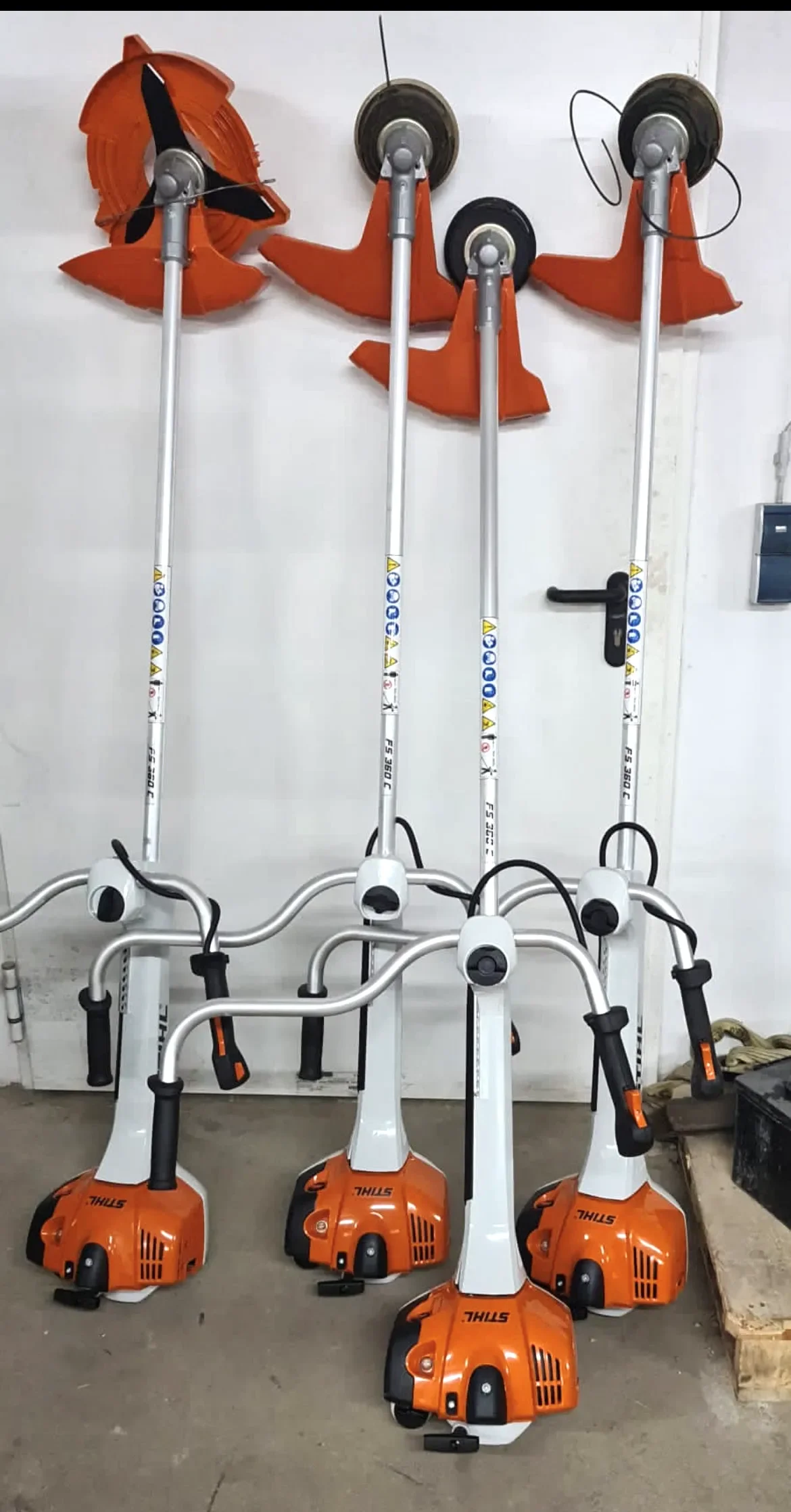 Mehrere orange-weiße benzinbetriebene Freischneider der Marke Stihl mit ergonomischem Zweihandgriff zur Miete für professionelle Mäh- und Ausputzarbeiten in zähem Gras und Gestrüpp.