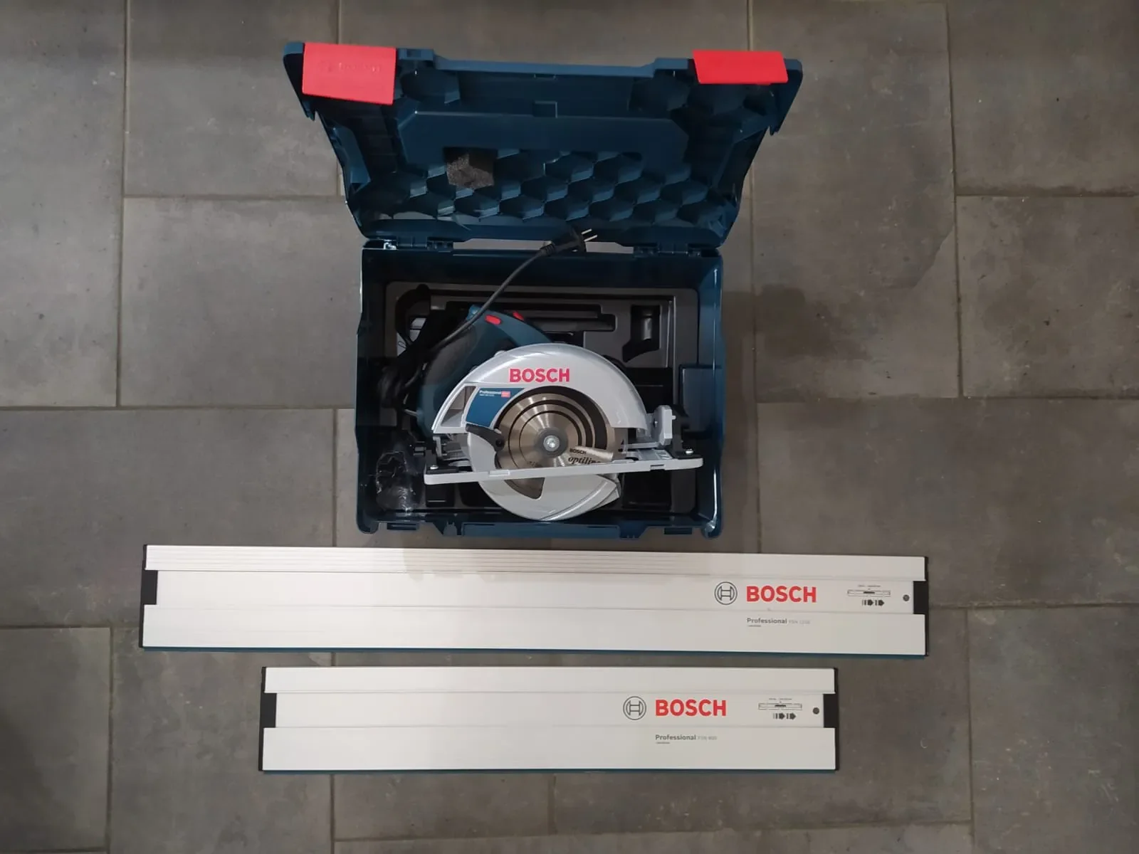 Hier ist der ALT-Text auf Deutsch:  Elektrische Handkreissäge der Marke Bosch Professional im geöffneten blauen Transportkoffer samt zwei unterschiedlich langen Führungsschienen aus Aluminium.
