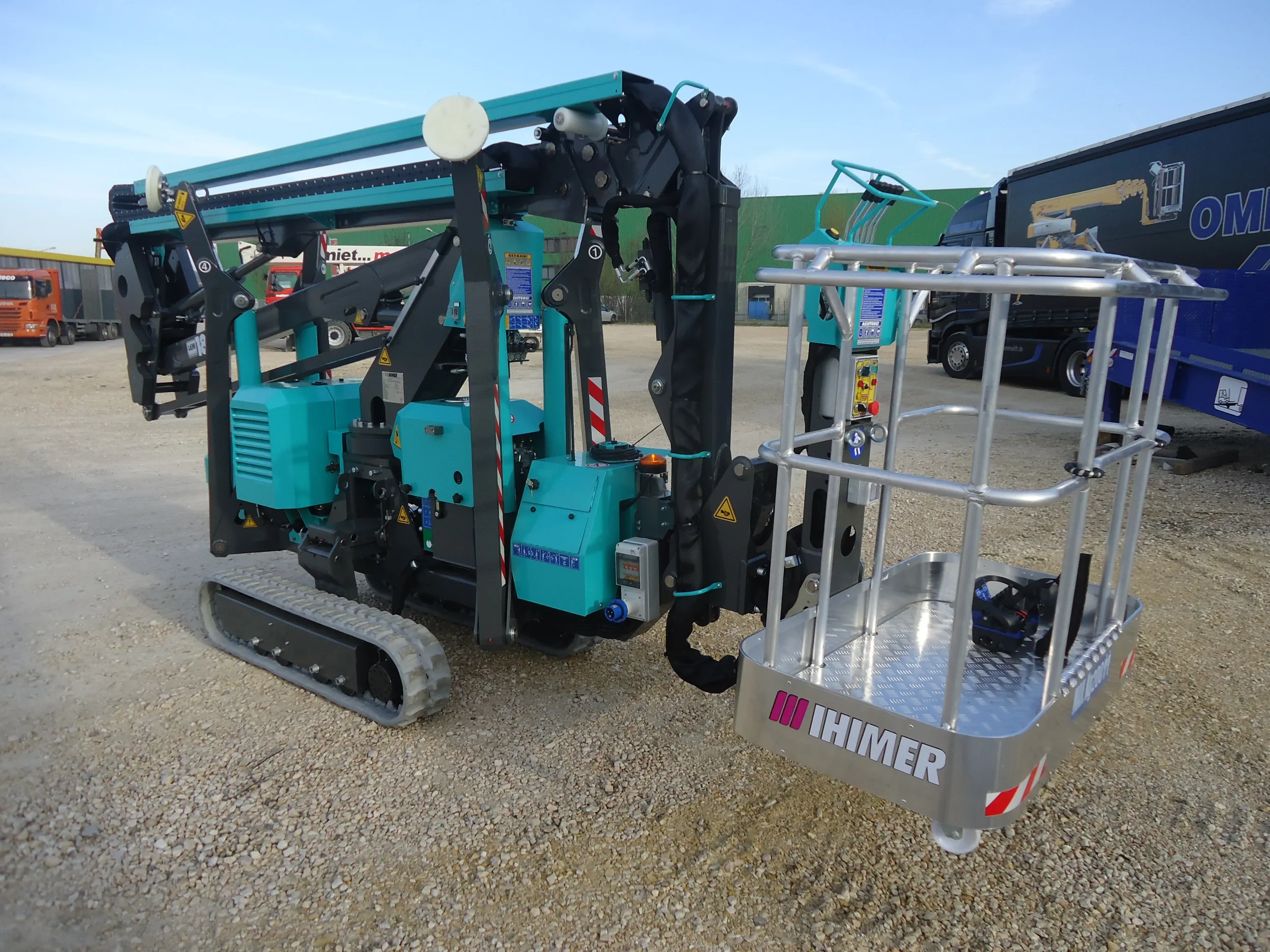 Türkise Raupenarbeitsbühne von IHMER mit Arbeitskorb auf einem Betriebshof.