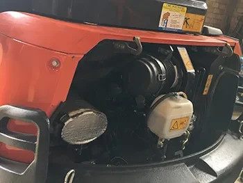 Offenes Motorfach einer roten Baumaschine mit sichtbarem Motor und Filtern, aufgenommen während Wartung und Reparatur.