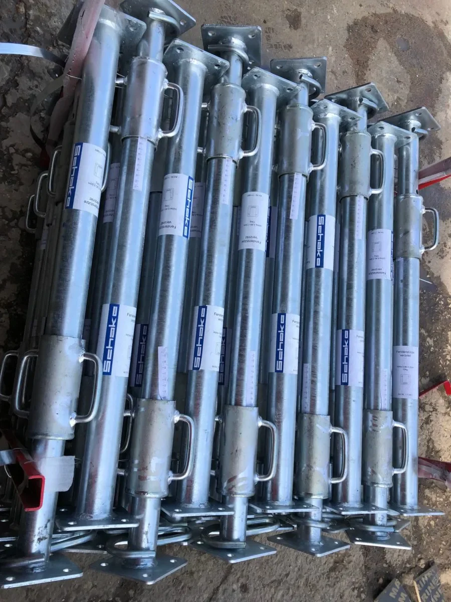 Mehrere gestapelte, verzinkte Fensterstützen (Kurzstützen) der Marke Schake aus Metall mit Kopf- und Fußplatte sowie stufenlosem Schraubgewinde zur Miete als Schalungszubehör für das sichere Abstützen von Fensterstürzen.