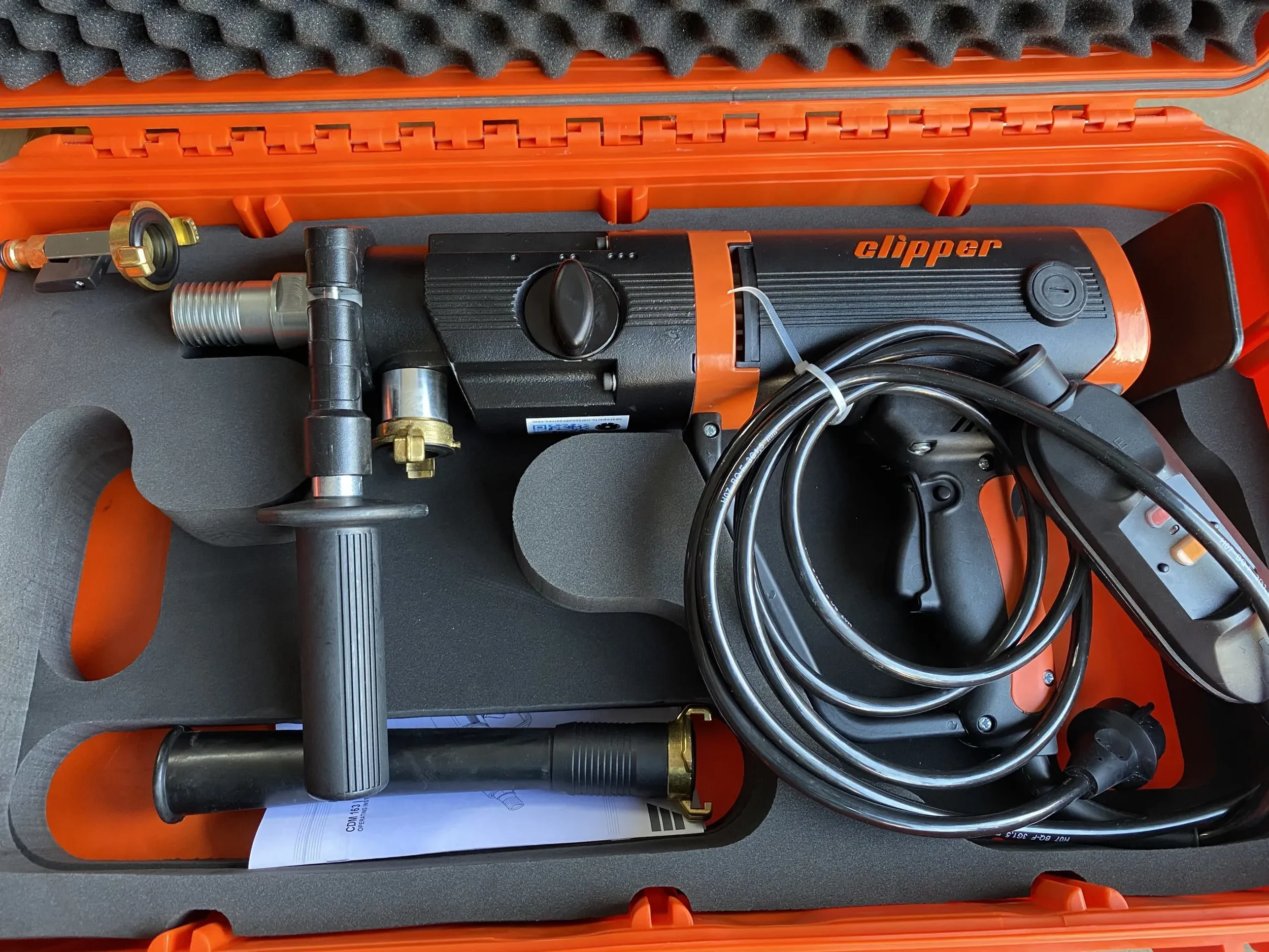 Handgeführtes elektrisches Kernbohrgerät der Marke Norton Clipper sicher verstaut im orangefarbenen Transportkoffer zur Miete für präzise Nass- und Trockenbohrungen in Mauerwerk und Beton.