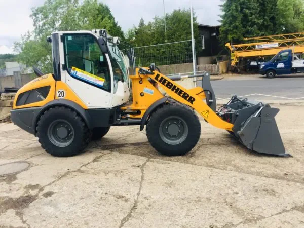 Hier ist der ALT-Text auf Deutsch:  Leistungsstarker, gelb-weißer Kompaktradlader der Marke Liebherr (Modell L 508 Compact) mit geschlossener Kabine und vielseitiger Klappschaufel zur Miete für effiziente Lade-, Transport.