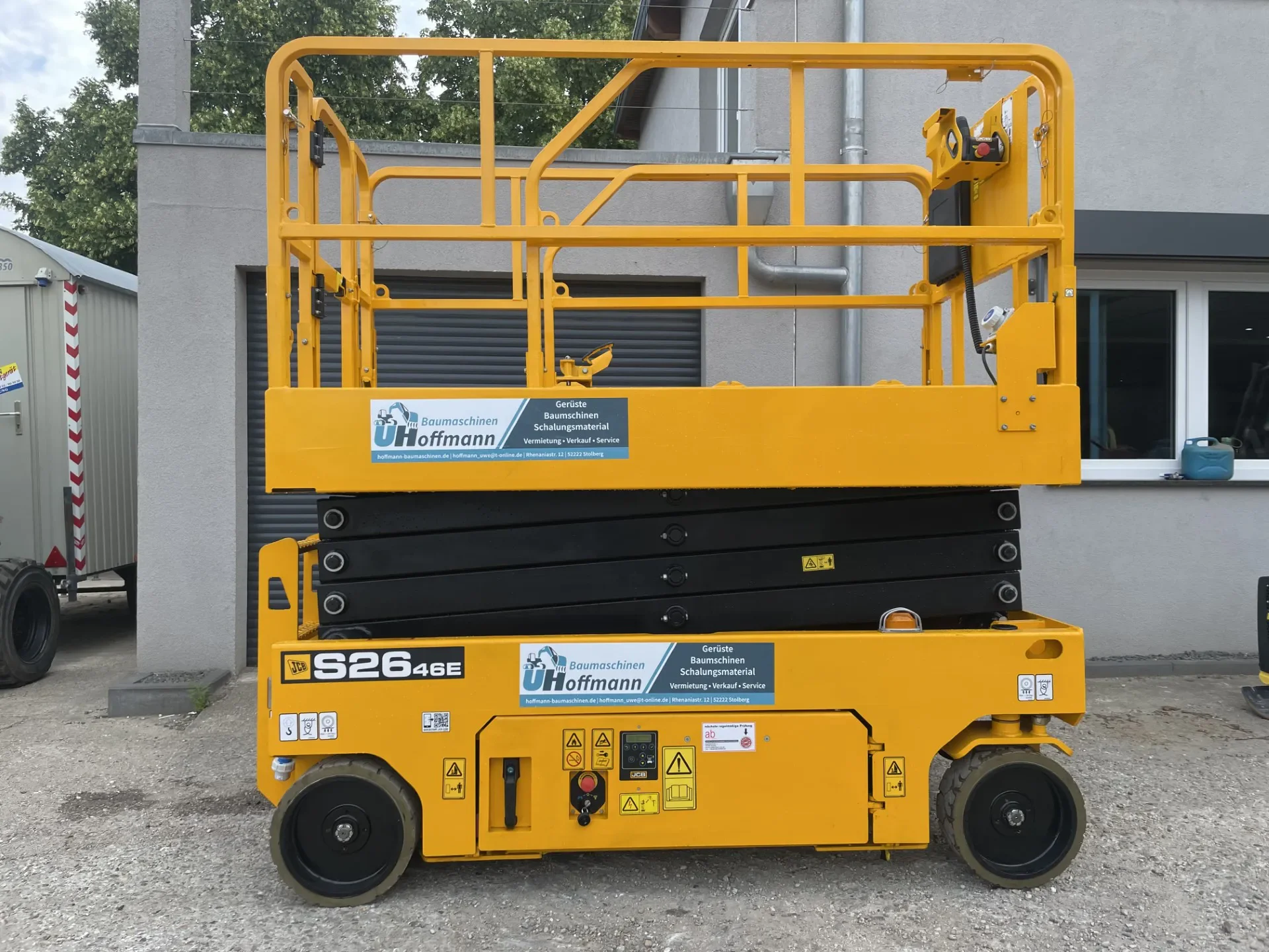 Gelbe JCB-Scherenarbeitsbühne mit Arbeitsplattform, abgestellt vor einem Gebäude.