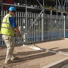 Manuelles Handabziehsystem mit langem Stiel und breitem Abziehprofil im Einsatz durch einen Bauarbeiter, zur Miete für das präzise und ergonomische Planieren von Sand und Splitt im Wege- und Pflasterbau.