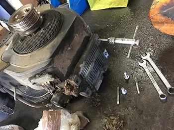 Ausgebauter Kleinmotor auf Werkstattboden neben Werkzeugen und Schrauben, während der Reparatur und Demontage.