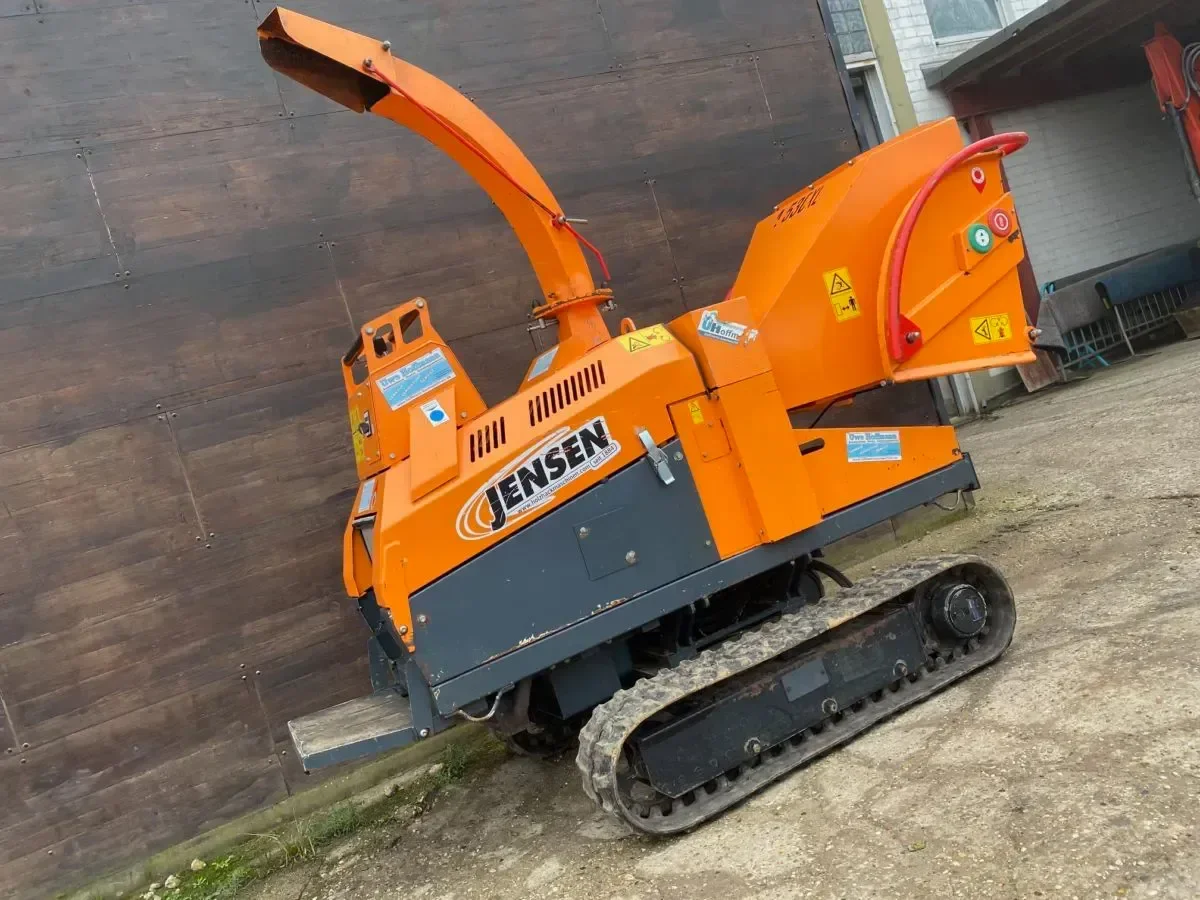 Orangefarbener Jensen A530XL Raupenhäcksler (Holzhäcksler) mit Auswurfkanal, seitliche Ansicht auf Betriebshof, Gebrauchtmaschine zum Verkauf.