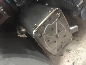 Nahaufnahme eines defekten Maschinenteils mit Metallgehäuse und angeschlossenen Schläuchen in einer Werkstatt, bereit für die Reparatur.