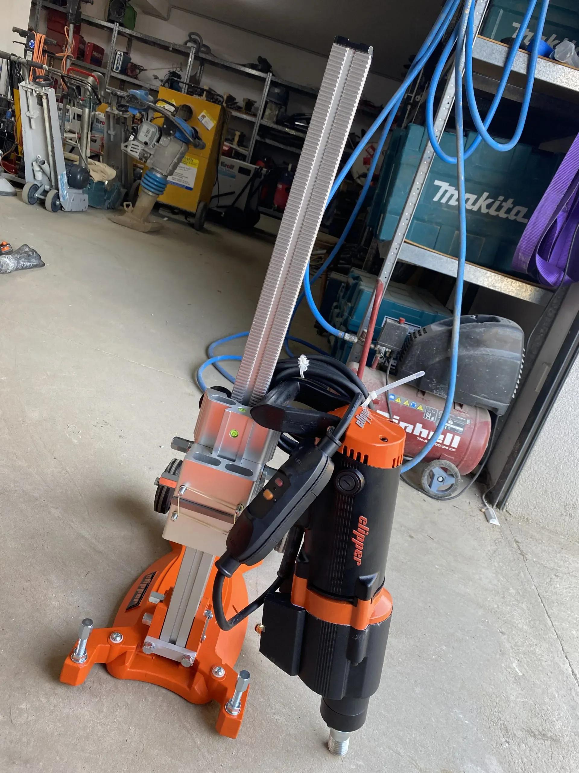 Hier ist der ALT-Text auf Deutsch:  Leistungsstarkes elektrisches Kernbohrgerät der Marke Norton Clipper, montiert auf einem stabilen Bohrständer, zur Miete für präzise, geführte und große Kernbohrungen in harten Materialien wie Beton oder Mauerwerk.