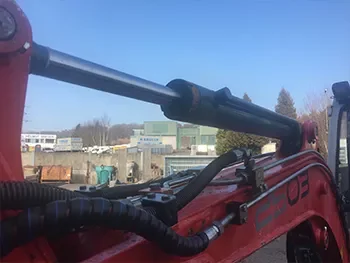 Ausleger einer roten Baumaschine mit sichtbarem Hydraulikzylinder und Leitungen, aufgenommen während einer Reparatur bzw. Inspektion.