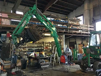 Werkstattansicht mit grünem Ladekran/Greifer und Werkbänken, während Reparatur- und Instandsetzungsarbeiten an Maschinen.