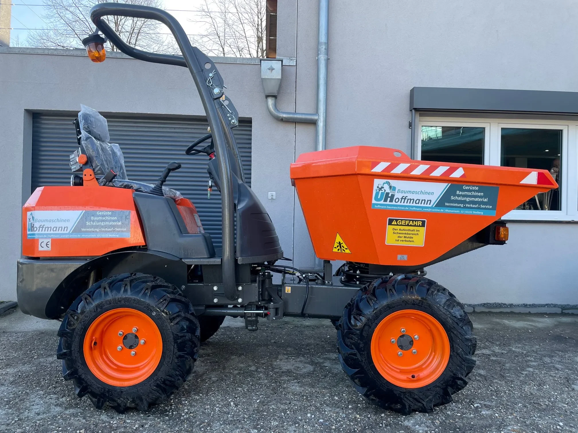 Orangefarbener, allradgetriebener Raddumper der Marke Ausa mit Fahrersitz, Überrollbügel und großer Frontkippmulde zur Miete für den schnellen und geländegängigen Transport von Erde, Schüttgut und Baumaterialien auf Baustellen.