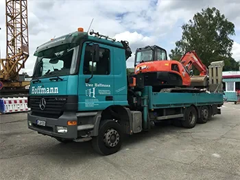 Tieflader-Lkw mit aufgeladener Baumaschine auf dem Firmengelände, aufgenommen im Rahmen von Transport und Werkstattservice.