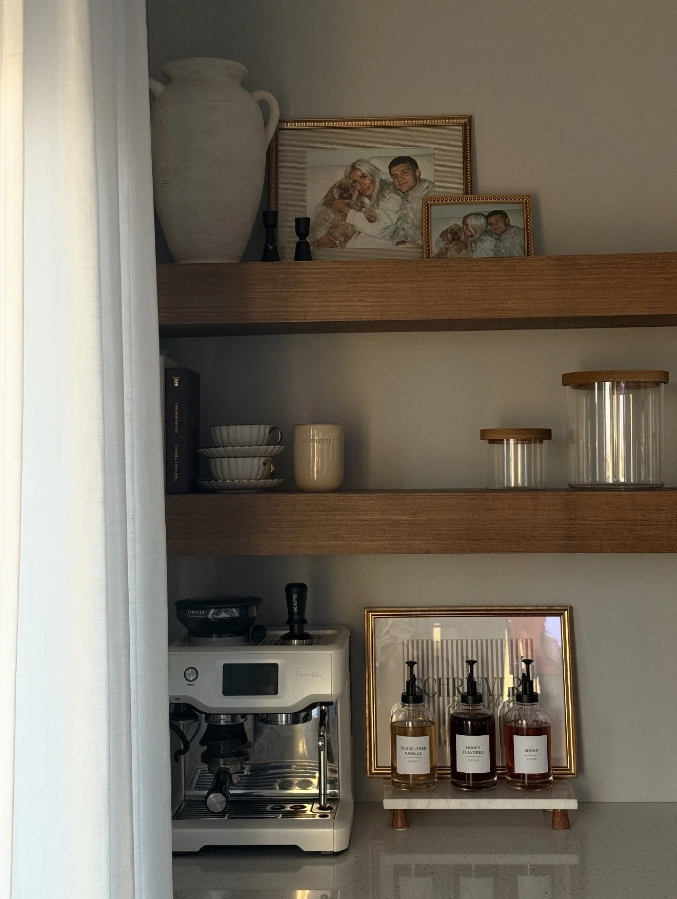 Kitchen shelf with framed family photos, decorative jars, cups, and a coffee machine.
