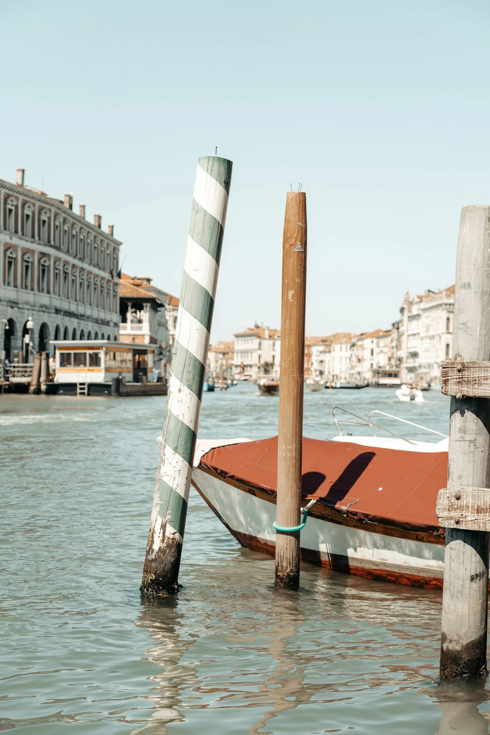 Boat docked at a canal with decorative striped poles on a sunny day in Venice, Italy.
