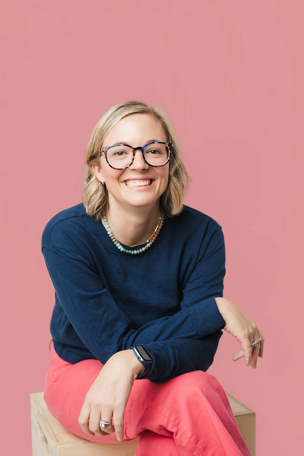 Jessica Whatley, founder of The Efficiency Choice, seated and smiling against a pink background