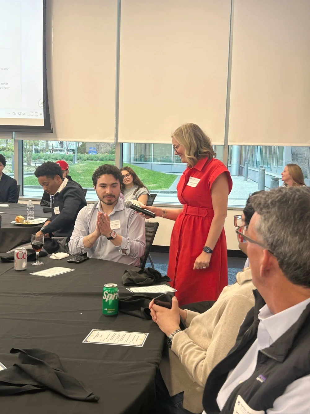 Jessica Whatley with a microphone at a table discussion, with participants sharing around the room