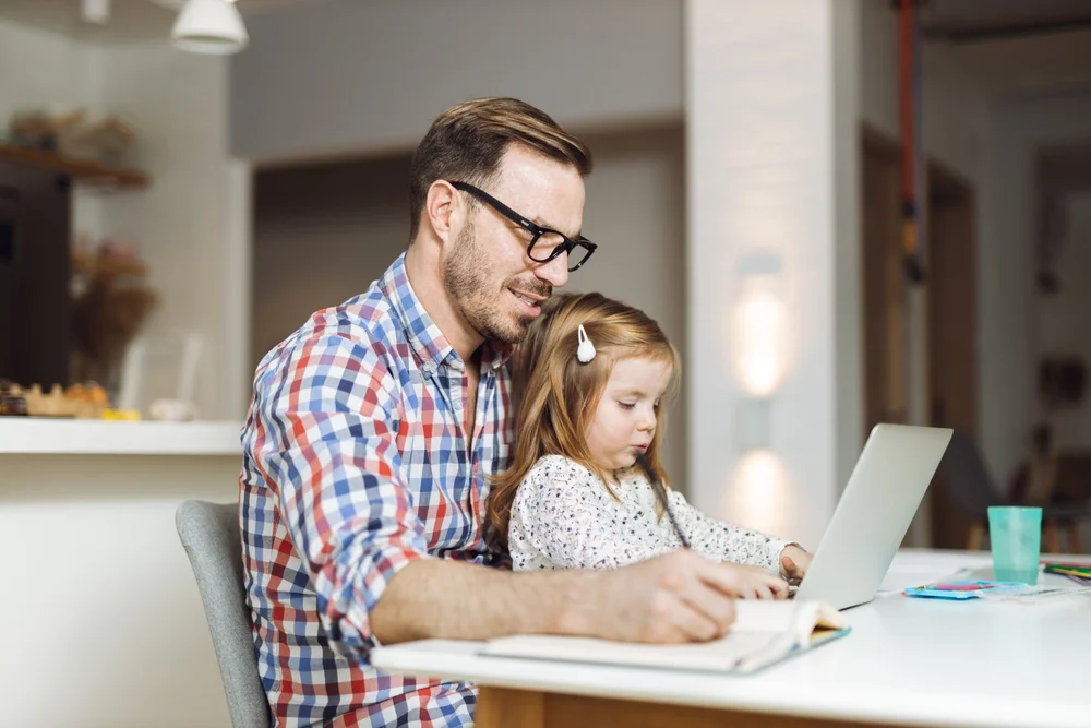 A dad working at his laptop with his young daughter on his lap