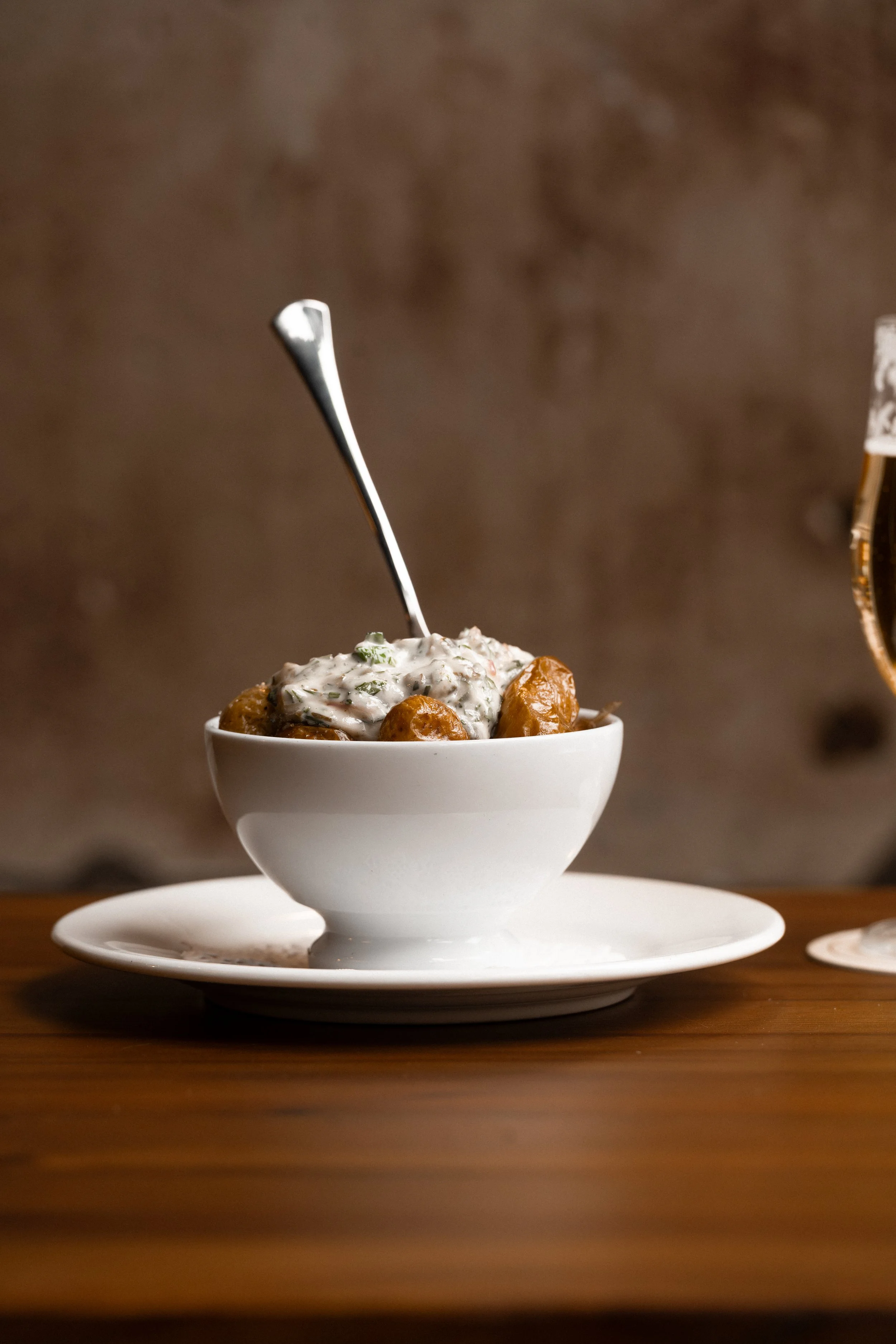 A white bowl filled with a crispy potatoes, topped with tartare, placed on a matching white saucer on a wooden table.