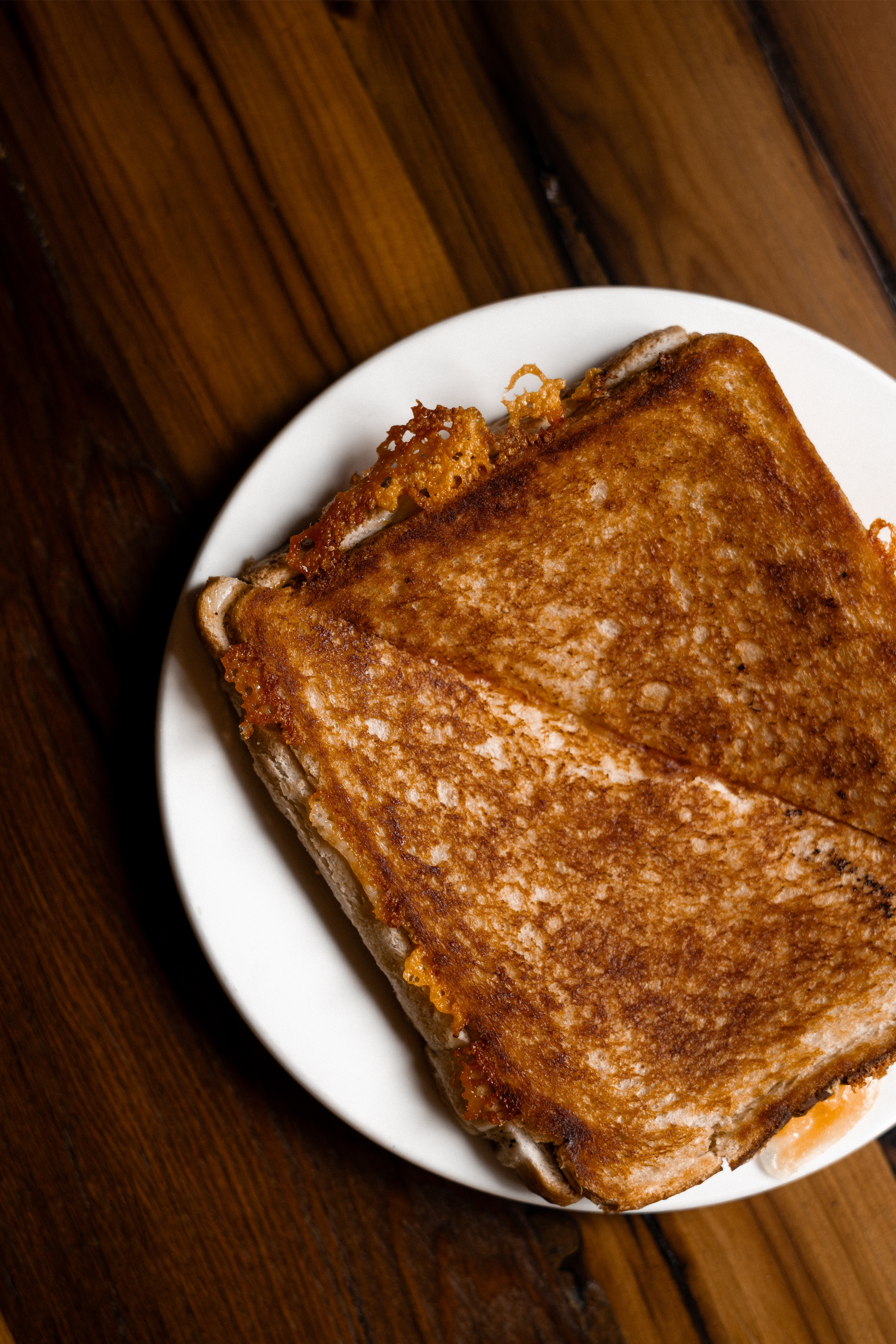 A toasted sandwich with melted cheese, placed on a white plate on a wooden table.