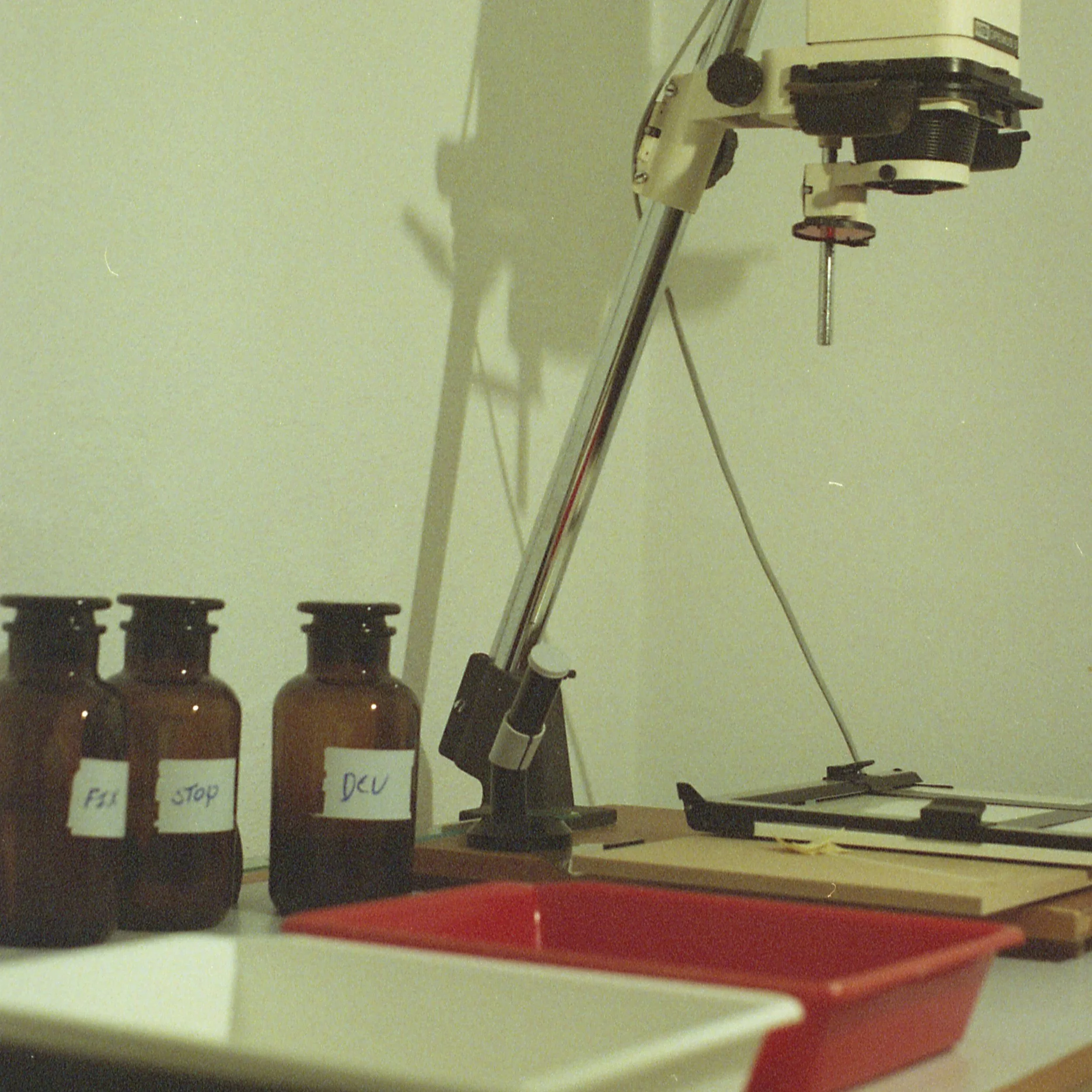 Darkroom equipment on a table including an enlarger and printing trays as well as bottles with chemicals.