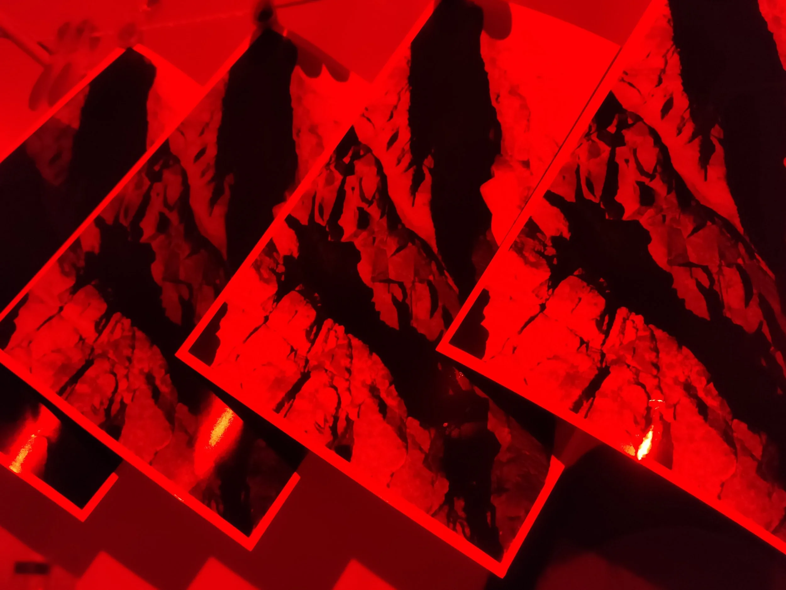 Multiple printed photographs of mountain landscapes with icy peaks, illuminated by red light, arranged in overlapping layers.