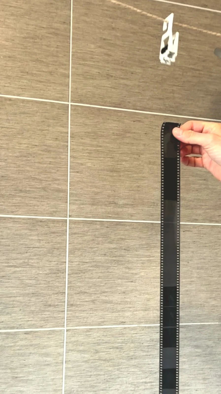 A person holding a strip of 35mm film in front of a tiled wall 