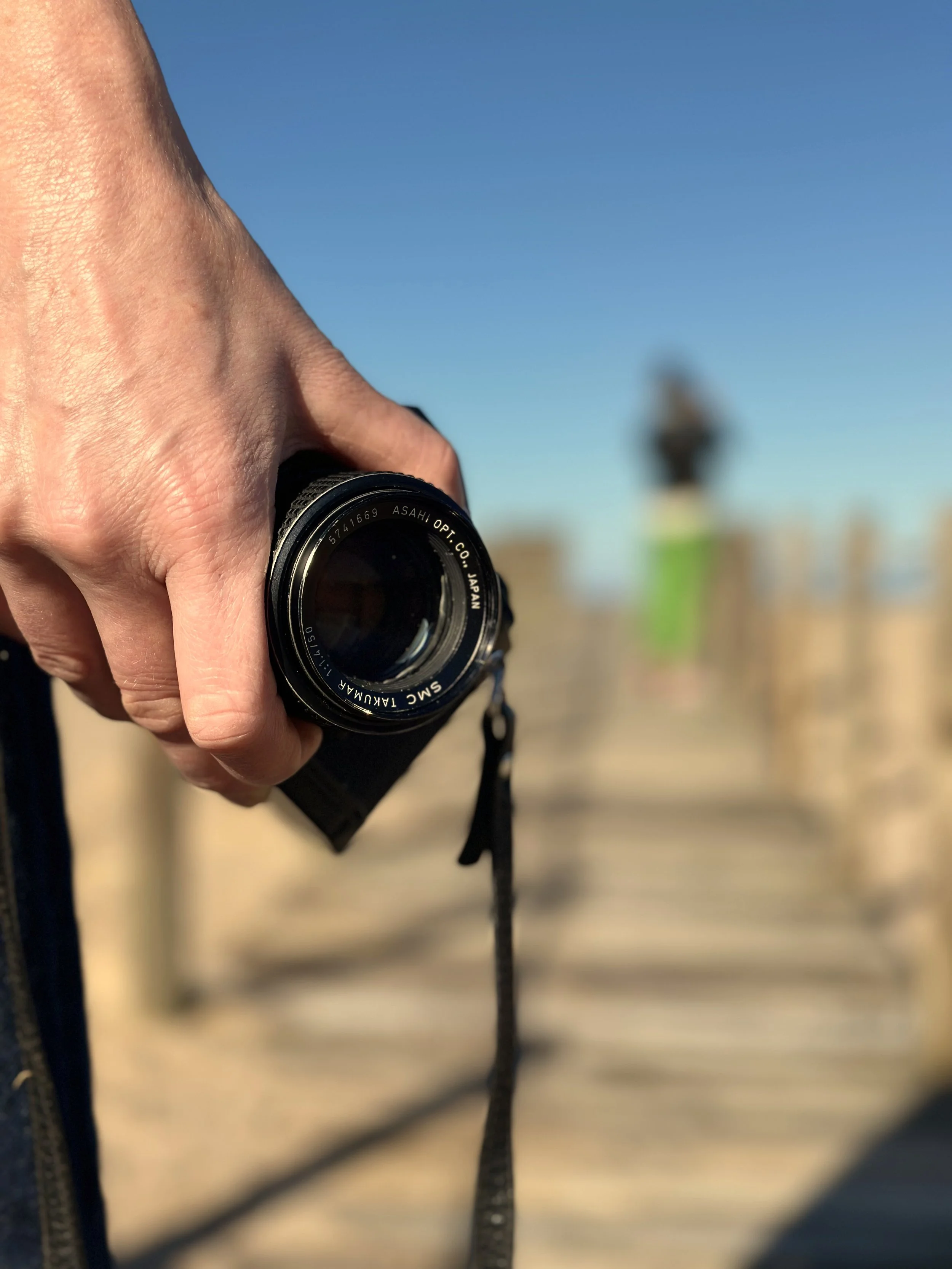 A person holding a camera with a beach and a lighthouse in the background.