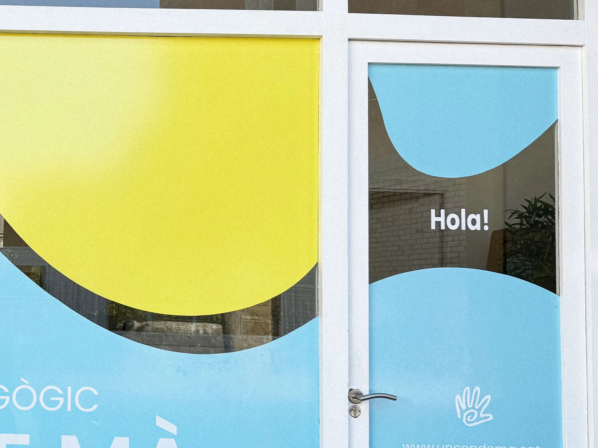 Puerta de vidrio decorada con formas en colores azul y amarillo, con la palabra 'Hola!' escrita en el centro de la puerta.