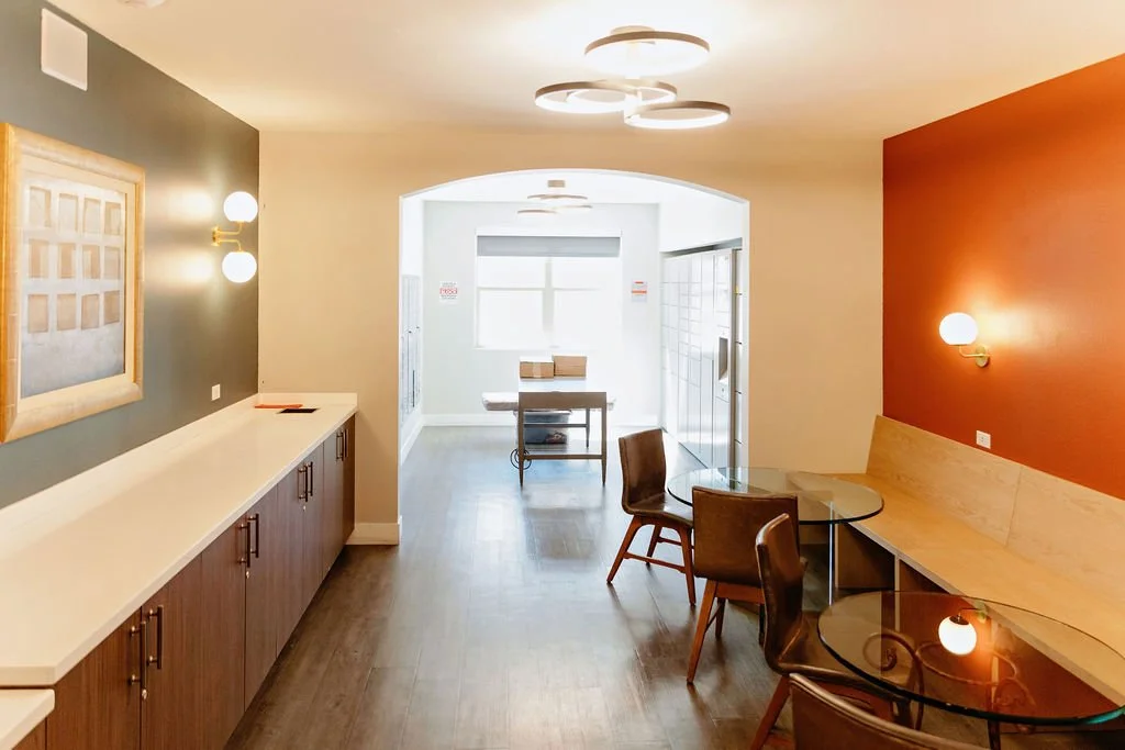 Interior of a modern cafe or communal space with tables, chairs, and contemporary lighting fixtures.